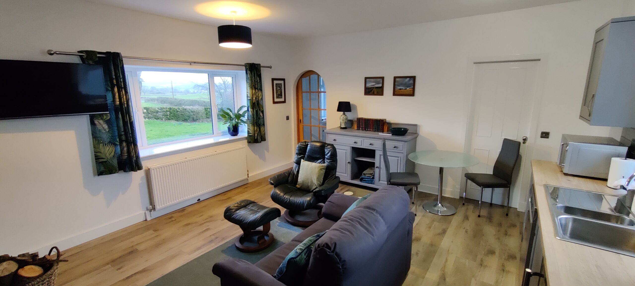 Kitchen Lounge, view from kitchen corner. Shows dining table and chairs, sofa and comfy chair, and TV
